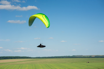Paragliding over the green field in summer sunny day. One paraglider fly over green field near...