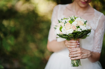 Close-up portrait of a stunning young bride holidng her bouquet in the forest.