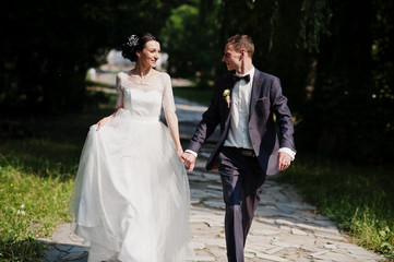 Fototapeta premium Gorgeous wedding couple holding hands and walking in the park on the sunny day.