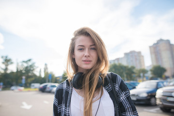 Attractive girl in casual clothing stands on the background of the city's landscape and looks at the camera. Street portrait of an attractive girl on a street in the city.