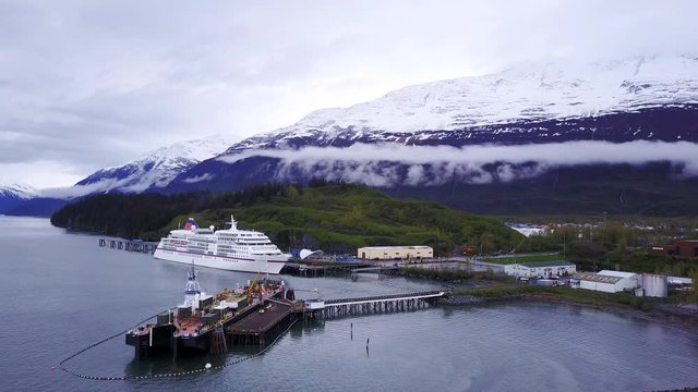Waterfront facilities with a cruise ship, barge landing with a band of fog in the background of mountains.
