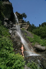 A young woman in a swimsuit is refreshed in the waterfall, Arkhyz.
