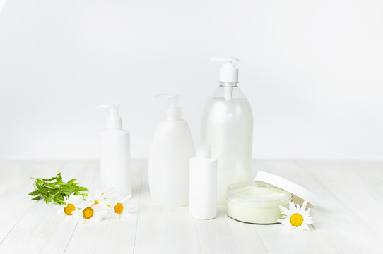 Opened plastic container with cream, white cosmetic bottle containers and chamomile flower on a white background. Herbal dermatology cosmetic hygienic cream Spa concept organic cosmetic 