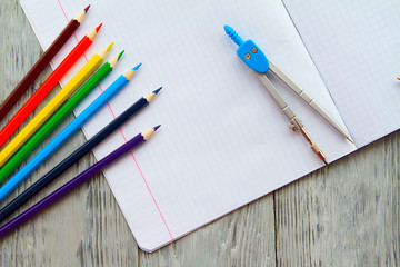 an open notebook on a wooden table lay next to colored pencils and compasses.