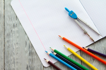 an open notebook on a wooden table lay next to colored pencils and compasses.