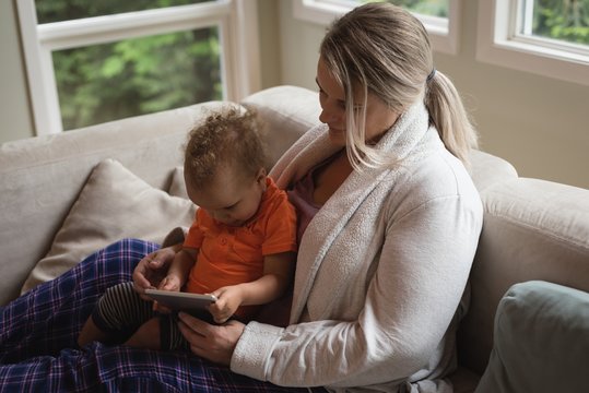 Mother and baby sitting on the sofa and using digital tablet
