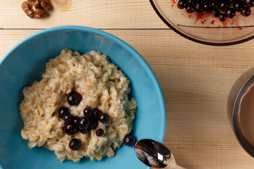Porridge in a bowl with the berries, walnuts and cocoa on bright wooden table. Healthy breakfast image. Top view with space