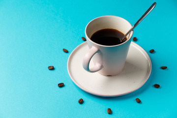 Coffee cup with spoon on saucer and coffee beans against blue background forming clock dial. Coffee as symbol of morning energy and cheerfulness or evening refreshment. Close up. Concept