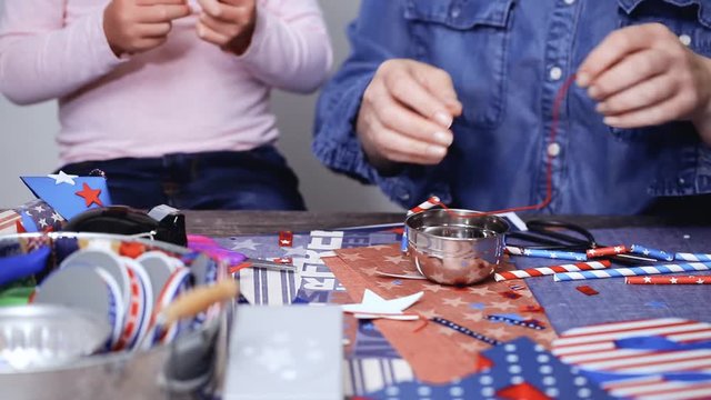 Step by step. Mother and daughter making neckles from paper straws and stars for July 4th celebration