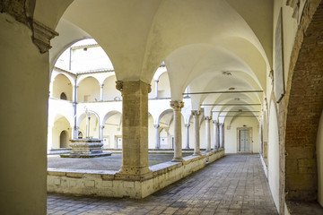 Fototapeta na wymiar Ancient Franciscan cloister with columns and capitals in Corinthian style. At the center is the well