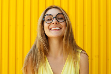 Portrait of a joyful girl wearing toy funny glasses looking up over yellow background at daylight