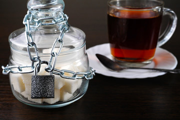 glass sugar bowl locked with chain and padlock with cup of tea on background