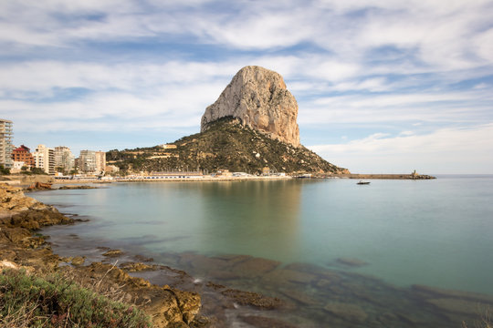 Ifach mountain from shoreline with peaceful Mediterranean sea and blue sky with white clouds