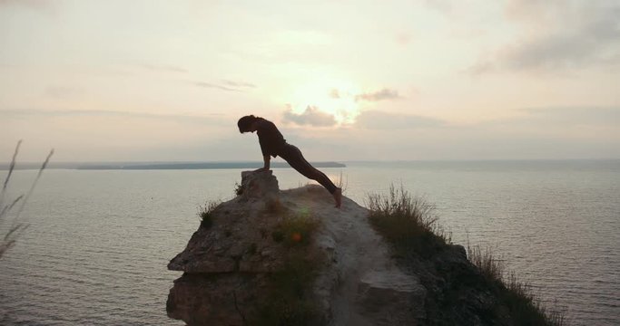 Young woman doing morning yoga on the big stone by the sea