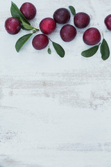 Fresh plums with leaves on white rustic wooden table background.