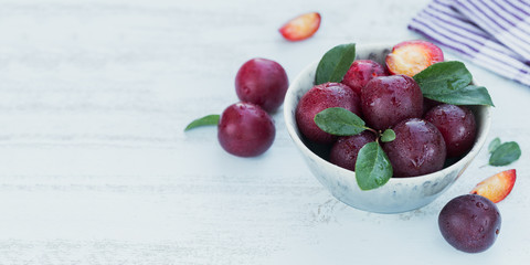 Fresh plums with leaves on rustic wooden table background.