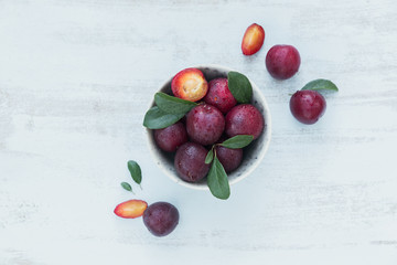 Fresh plums with leaves on rustic wooden table background.