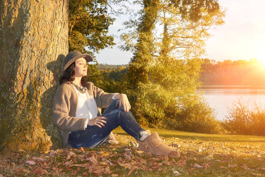 Woman Sitting Leaning On Tree In Fall Park