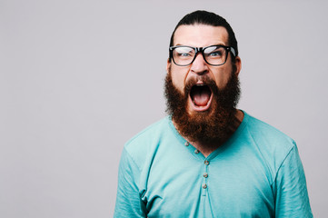 Obraz premium Young bearded man yelling and looking at the camera on white background.