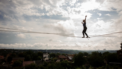 Young woman walking on the slackline rope on the bending knees - obrazy, fototapety, plakaty