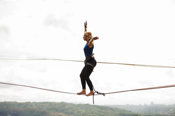 Young woman standing on the slackline rope on the bending knees - obrazy, fototapety, plakaty