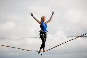 Young smiling woman standing with arms raised on the slackline rope