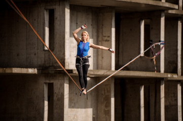 Obraz na płótnie Canvas Female equilibrist standing with one arm raised and other to the right on the slackline rope