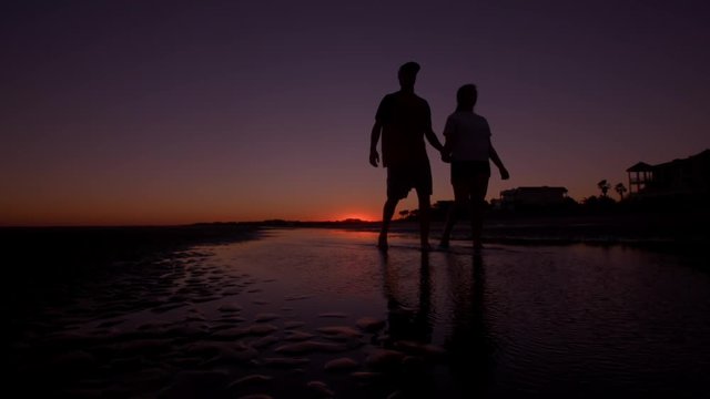 A silhouette of a young couple taking a romantic walk down the beach.