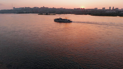 Aerial view of the ship sailing on the river in the city at sunset.