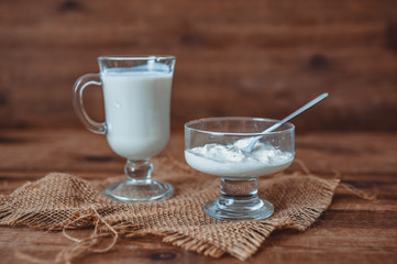 a glass of kefir and a cup with sour cream on a wooden background