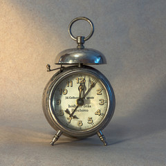 Old alarm clock in yellow light showes five past twelve