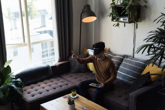 Man in virtual reality headset using digital tablet in living
