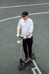 Modern man in stylish black and white outfit riding electric scooter in the city