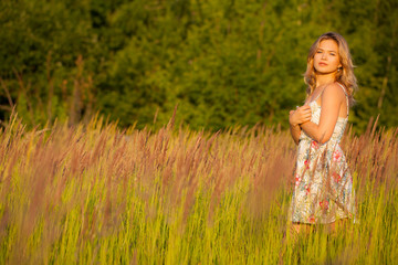 Fototapeta na wymiar Beautiful young woman standing in a field, green grass and flowers. Outdoors Enjoy nature. Healthy smiling girl standing in tall grass