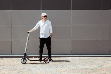Modern man dressed white shirt and black pants standing at the street with electric scooter