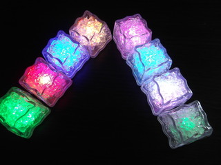 Bright and beautiful colors of different luminous ice cubes on a dark wooden background