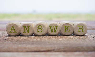 Answer word written on cube shape wooden blocks on wooden table.