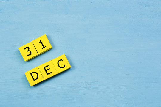 DEC 31, yellow cube calendar on blue wooden surface with copy space