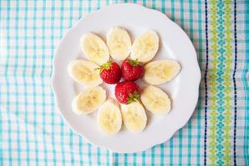 banana and strawberries on a white plate and a colorful napkin.