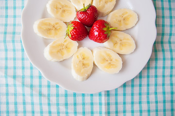 banana and strawberries on a white plate and a colorful napkin.