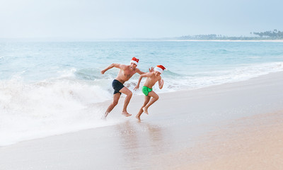 Father and son have a fun on ocean beach, run away from big waves. Christmas holiday time. Tropical vacation