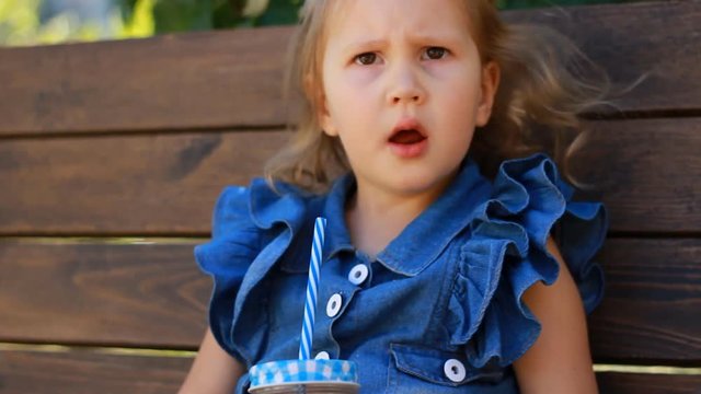 Child girl drinks smoothies in the park on a sunny day. Close up