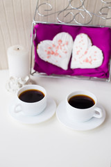 two cups of coffee, cookies and candle in the form of heart on a pink napkin.