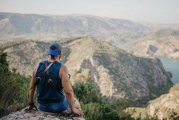 Fototapeta premium Lonely man in the blue shirt and shorts sitting on the stone above the ancient canyon in Spain on the sunset 
