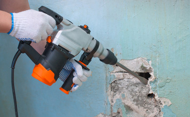 The builder with hammer drill perforator equipment making hole in wall at construction site.