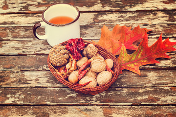 Autumn tea in white vintage cup, red chili peppers, walnuts, chestnut and conch in a wooden bowl on old rustic wooden table with autumn leaves.
