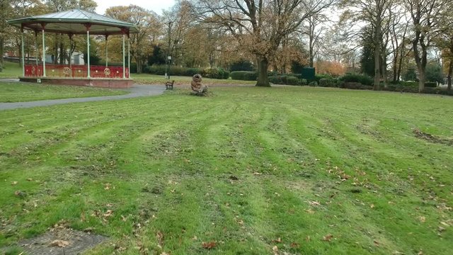 Moving towards a Victorian bandstand & wooden lion sculpture artwork in the park.