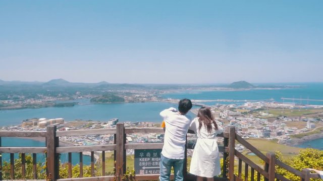 a couple is standing and pointing out over jeju island in South Korea traveling