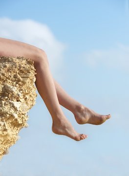 Woman's legs dangling over the edge of a rock