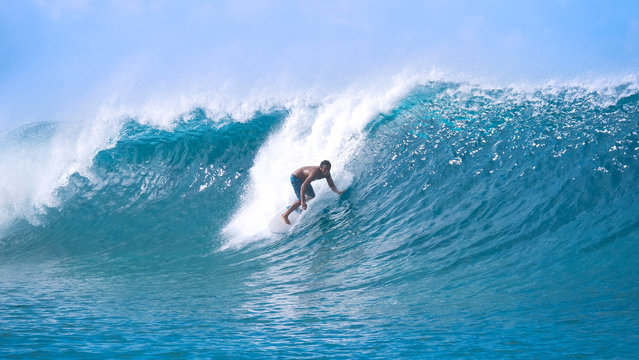 Carefree young sportsman on summer vacation surfing a breathtaking barrel wave.